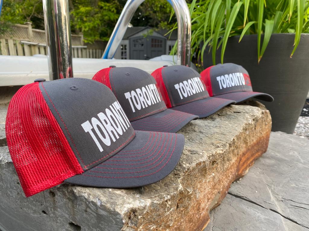 Toronto Jet Ski Trucker Hat: Front panel in grey with white embroidered 'Toronto' and red 'jetski' logo. Back features breathable red mesh material. Red stitching accents the brim, adding a coordinated touch to this stylish watersport accessory.